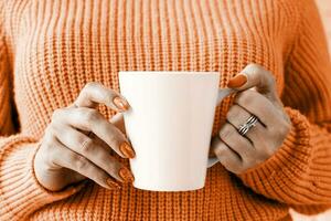 Color of the year 2024, Peach Fuzz. closeup woman hands holding white mug for mockup design photo