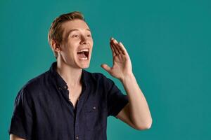 Close-up portrait of a ginger guy in navy t-shirt posing on blue background. Sincere emotions. photo