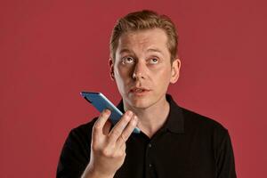 Close-up portrait of a ginger guy in black t-shirt posing on pink background. Sincere emotions. photo