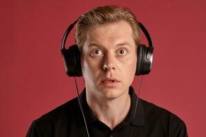 Close-up portrait of a ginger guy in black t-shirt posing on pink background. Sincere emotions. photo