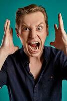 Close-up portrait of a ginger guy in navy t-shirt posing on blue background. Sincere emotions. photo