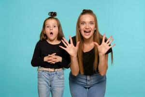 Mom and daughter with a funny hairstyles, dressed in black shirts and blue denim jeans are posing against a blue studio background. Close-up shot. photo