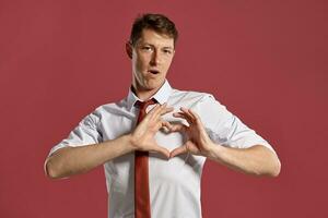 Young man in a classic white shirt and red tie posing over a pink background. photo