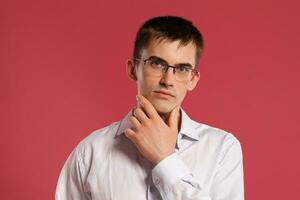 Young man in a classic white shirt is posing over a pink background. photo