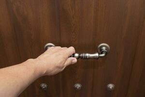 A hand holding the decorative metal bracket of a wooden door. The entrance of a house. photo