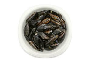 Raw mussels in a white bowl, isolated on white background. It feeds on phytoplankton and zooplankton, and even decomposing organic particles found in seawater, by filtering it through its gills. photo