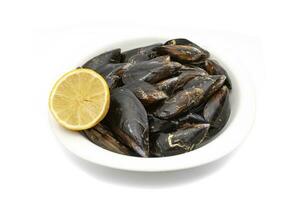Raw mussels in a white bowl, isolated on white background. It feeds on phytoplankton and zooplankton, and even decomposing organic particles found in seawater, by filtering it through its gills. photo