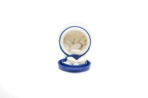 A container with pills. Open blue lid, seeing the white pills inside the container and outside. A tablet is a solid pharmaceutical form that contains one or more active ingredients. photo