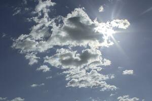 A blue sky with white clouds, coming out some rays of sun, as a background. photo