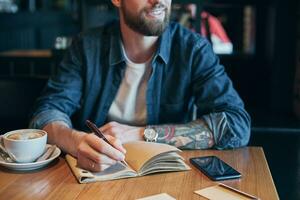 Man hand with pen writing on notebook on a wooden table. Close-up photo