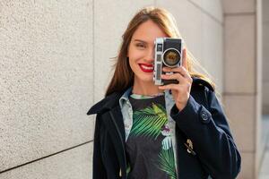 Happy hipster girl making photo with retro camera on city street