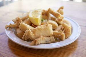 Fried cuttlefish strips, called Chocos Fritos in Spanish. It is served on a white plate on a wooden table. Spanish food concept. photo