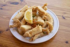 Fried cuttlefish strips, called Chocos Fritos in Spanish. It is served on a white plate on a wooden table. Spanish food concept. photo