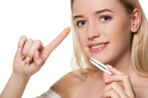 Young woman holding tweezers for contact lenses and lens in front of her face on white background photo