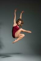 Beautiful woman dancer wearing maroon swimsuit posing on a grey studio background photo