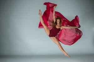 Young beautiful woman dancer in red swimsuit posing on a light grey studio background photo