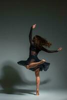 Young beautiful dancer in black dress posing on a dark gray studio background photo