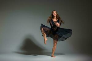 Young beautiful dancer in black dress posing on a dark gray studio background photo