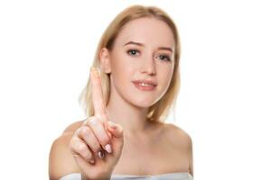 Focus on contact lens on finger of young woman. Young woman holding contact lens on finger in front of her face. Woman holding contact lens on white background. photo