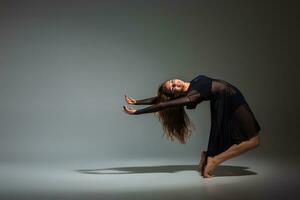 Young beautiful dancer in black dress posing on a dark gray studio background photo