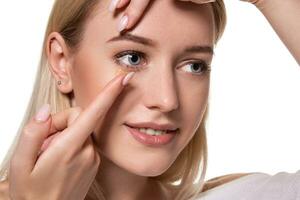 Young woman holding contact lens on index finger with copy space. Close up face of healthy beautiful woman about to wear contact lens. photo