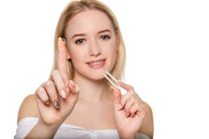 Focus on contact lens on finger of young woman. Young woman holding contact lens on finger in front of her face. Woman holding contact lens on white background. photo