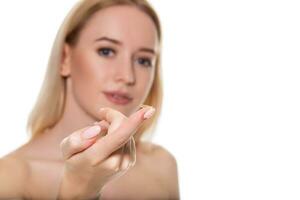 Focus on contact lens on finger of young woman. Young woman holding contact lens on finger in front of her face. Woman holding contact lens on white background. photo