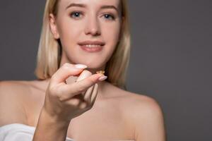 Focus on contact lens on finger of young woman. Young woman holding contact lens on finger in front of her face. Woman holding contact lens on grey background. photo