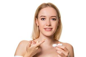 Young woman holding contact lenses cases and lens in front of her face on white background photo