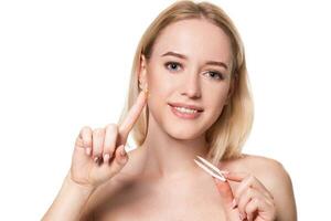 Young woman holding tweezers for contact lenses and lens in front of her face on white background photo