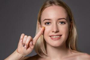 Young woman holding contact lens on index finger with copy space. Close up face of healthy beautiful woman about to wear contact lens. photo