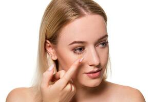 Young woman holding contact lens on index finger with copy space. Close up face of healthy beautiful woman about to wear contact lens. photo