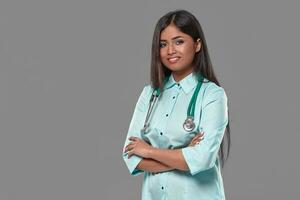 Adorable indian female doctor nurse with stethoscope in aquamarine dress on grey background photo