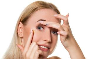 Young woman holding contact lens on index finger with copy space. Close up face of healthy beautiful woman about to wear contact lens. photo