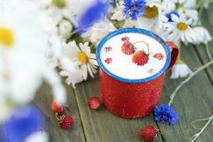 Fresco fresa con frío Leche en rojo jarra en salvaje flores fondo, infancia foto