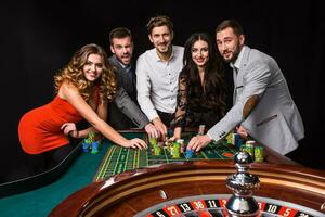 Group of young people behind roulette table on black background photo