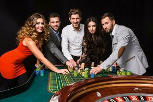 Group of young people behind roulette table on black background photo