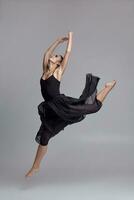 bailando bailarina en un negro vestido. contemporáneo agraciado actuación en un gris antecedentes. foto