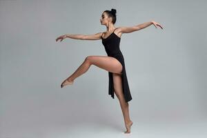 Dancing ballerina in a black dress. Contemporary graceful performance on a gray background. photo