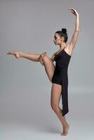 bailando bailarina en un negro vestido. contemporáneo agraciado actuación en un gris antecedentes. foto