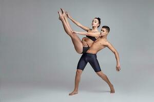 The couple of a young modern ballet dancers in black suits are posing over a gray studio background. photo