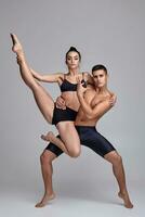 The couple of a young modern ballet dancers in black suits are posing over a gray studio background. photo