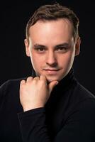 Studio shot of young man looking at the camera on black background. Vertical format, he has a serious face, he is wearing a black pullover. photo