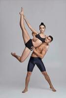 The couple of a young modern ballet dancers in black suits are posing over a gray studio background. photo