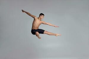 foto de un hermoso hombre ballet bailarín, vestido en un negro bermudas, haciendo un danza elemento en contra un gris antecedentes en estudio.