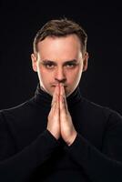 Studio shot of young man looking at the camera on black background. Vertical format, he has a serious face, he is wearing a black pullover. photo