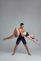 The couple of a young modern ballet dancers in black suits are posing over a gray studio background. photo