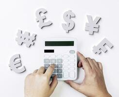 Exchange rates and bank foreign currency calculations. Top view of hands using calculator to perform calculations with currency symbols on white table photo