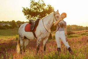 Jockey young girl petting and hugging white horse in evening sunset. Sun flare photo