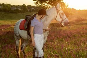 Jockey young girl petting and hugging white horse in evening sunset. Sun flare photo